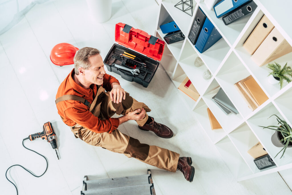 top view of repairman sitting on floor with injured knee in office