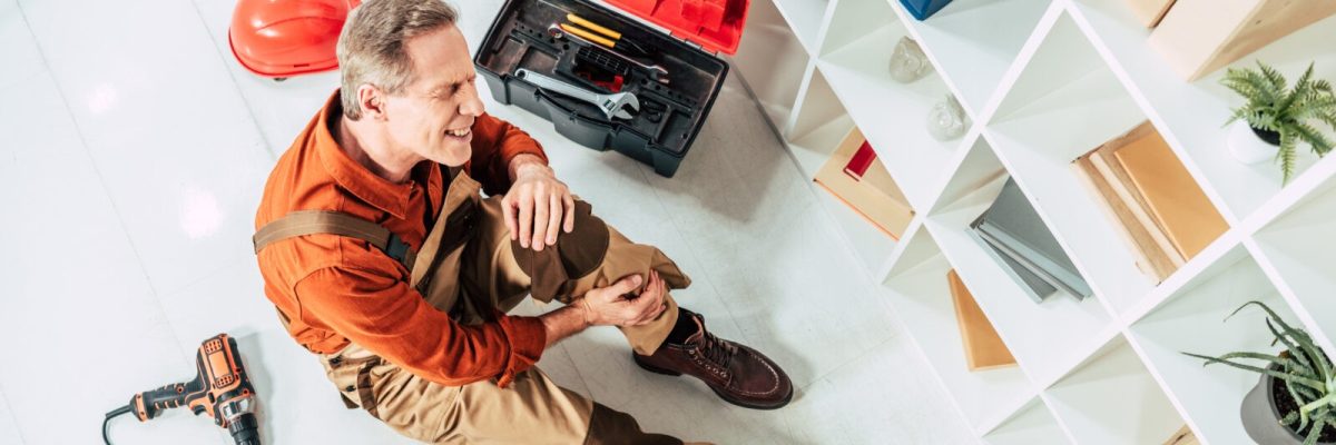 top view of repairman sitting on floor with injured knee in office